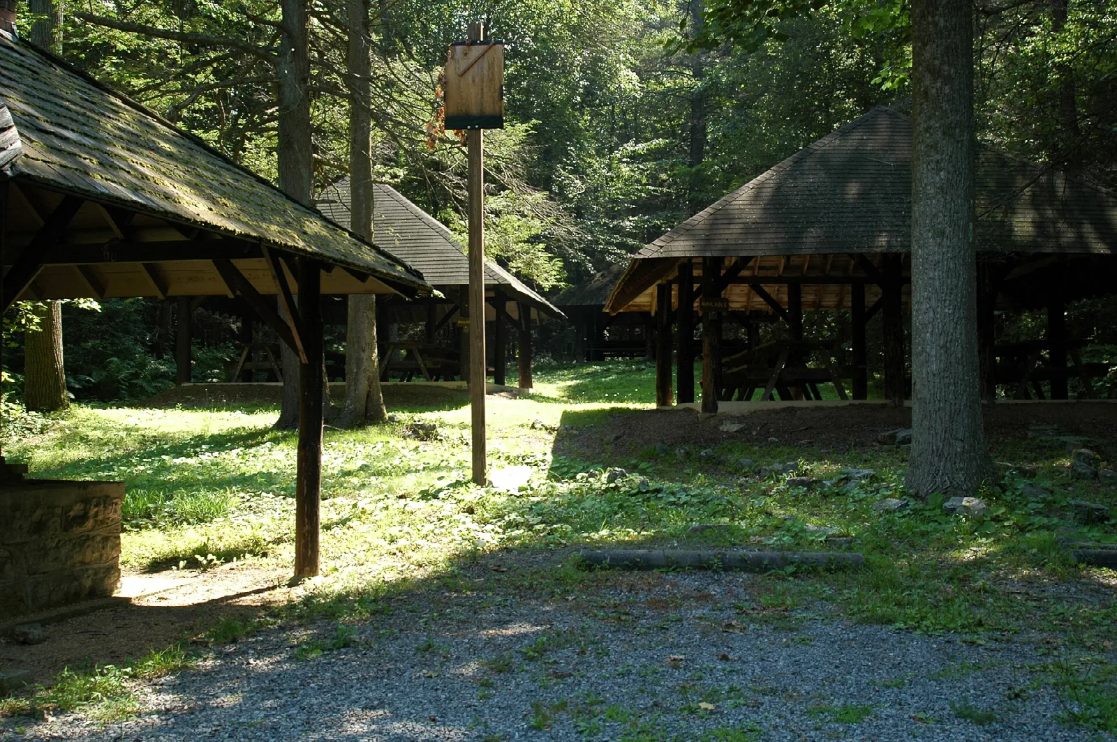 Wooden picnic shelters in a shaded grove with a gravel lane