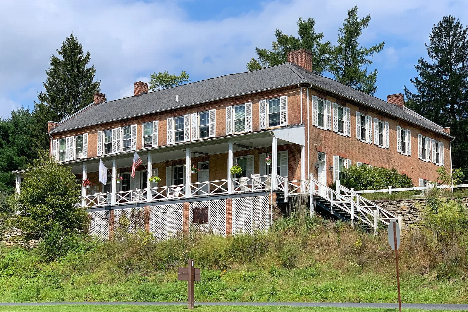 Long brick mansion with a porch among evergreens