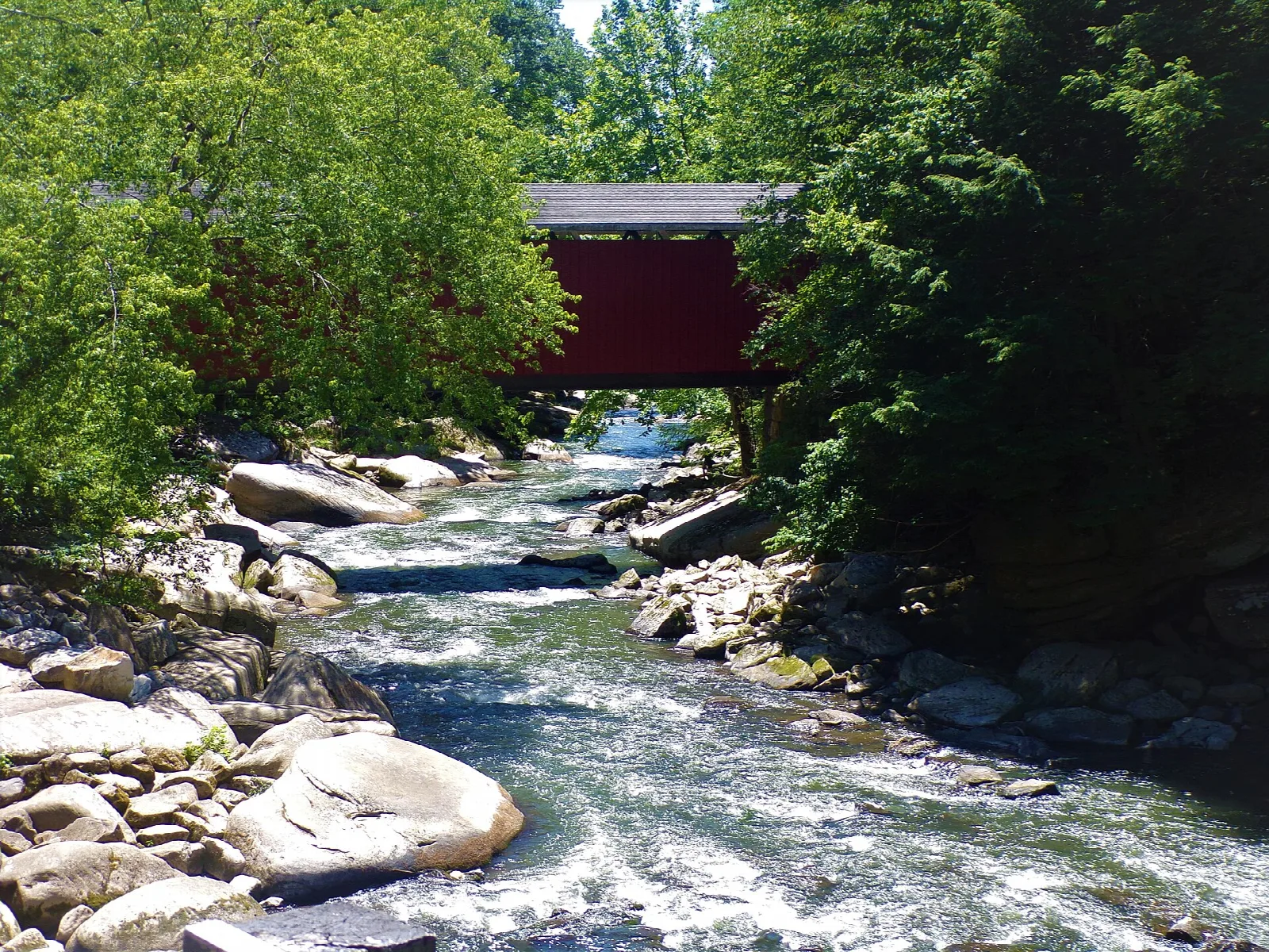 Rocky creek flowing toward a red covered bridge