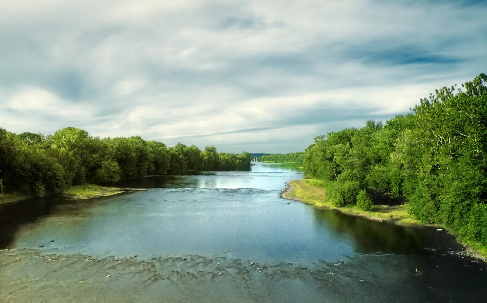 Wide river bending between tree-lined shores under cloudy sky