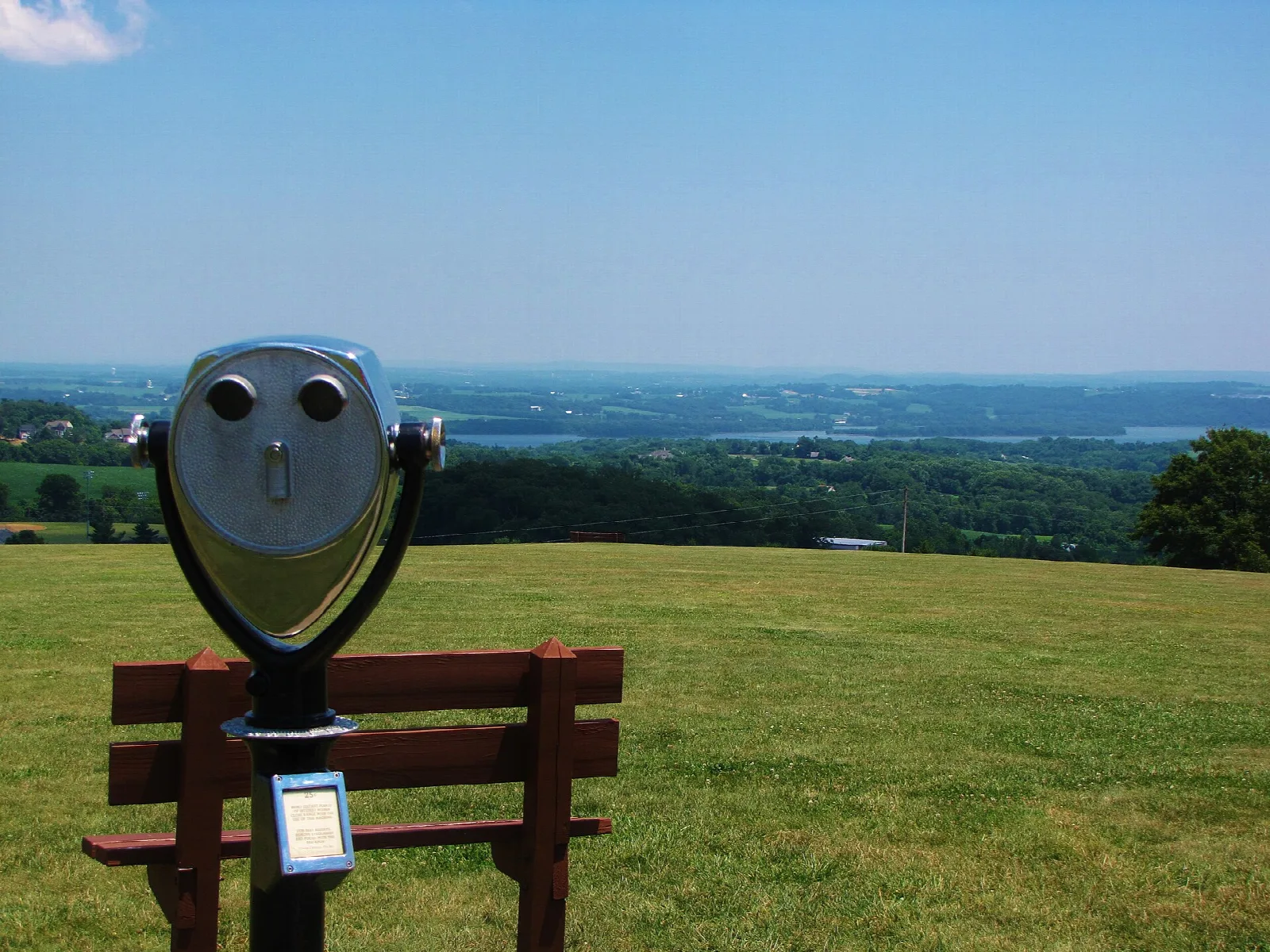 Coin-operated binoculars beside a bench on a grassy hilltop