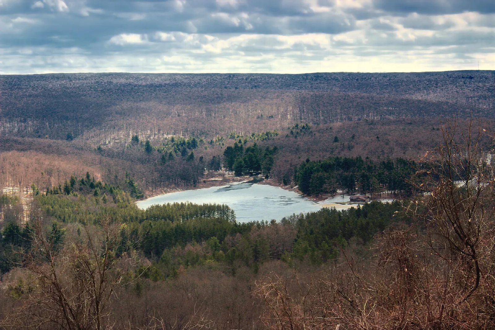 Wide view over a lake and wooded plateau under a cloudy sky
