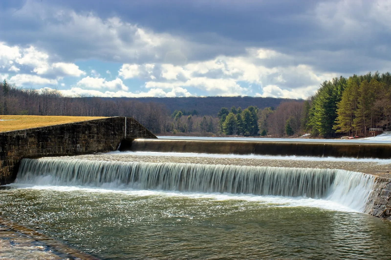Water spilling over a long stone dam with forest behind