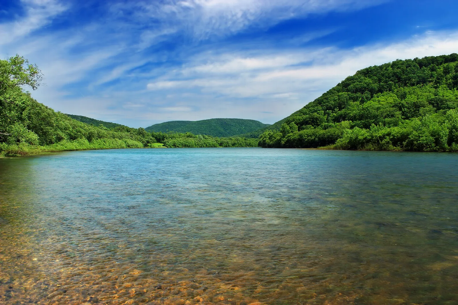 Clear shallow river bending between forested hills under blue sky