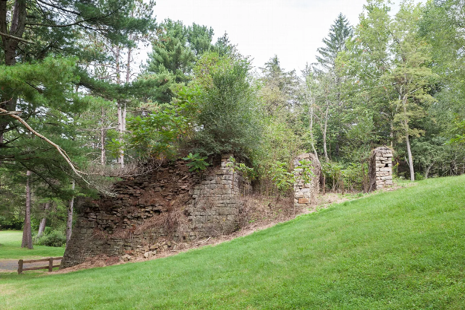 Weathered stone furnace stack on a grassy lawn among trees