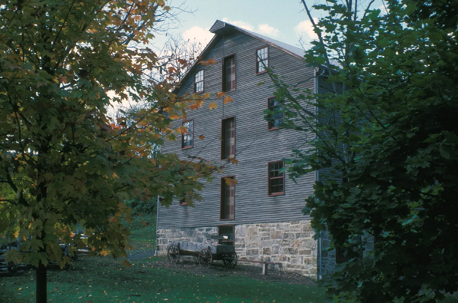 Gray wooden grist mill with a stone base among trees