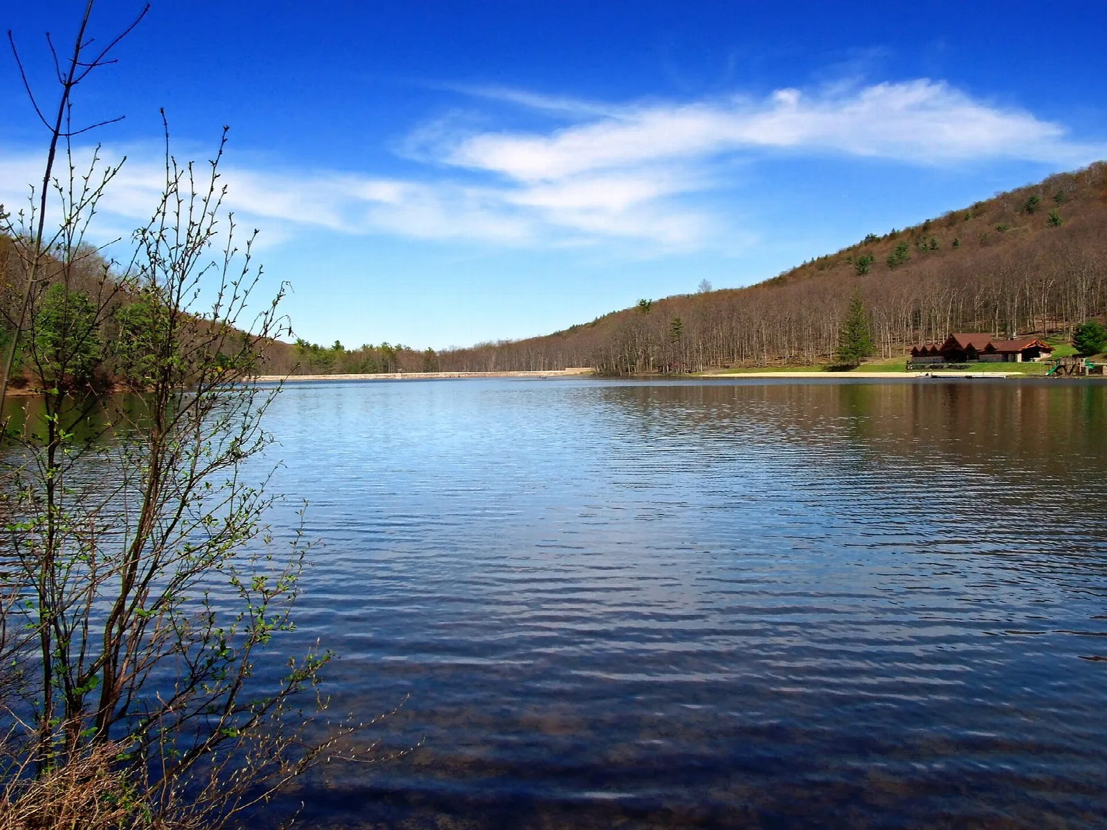Blue lake below a wooded hillside with a building on the far shore