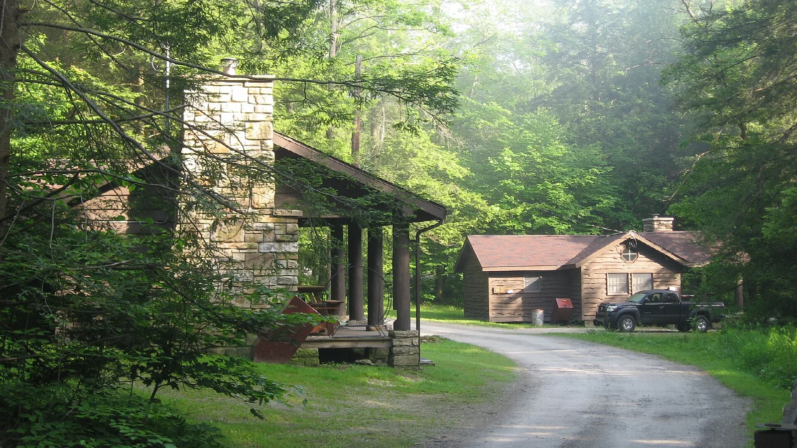 Two stone and log cabins in misty woods beside a gravel road