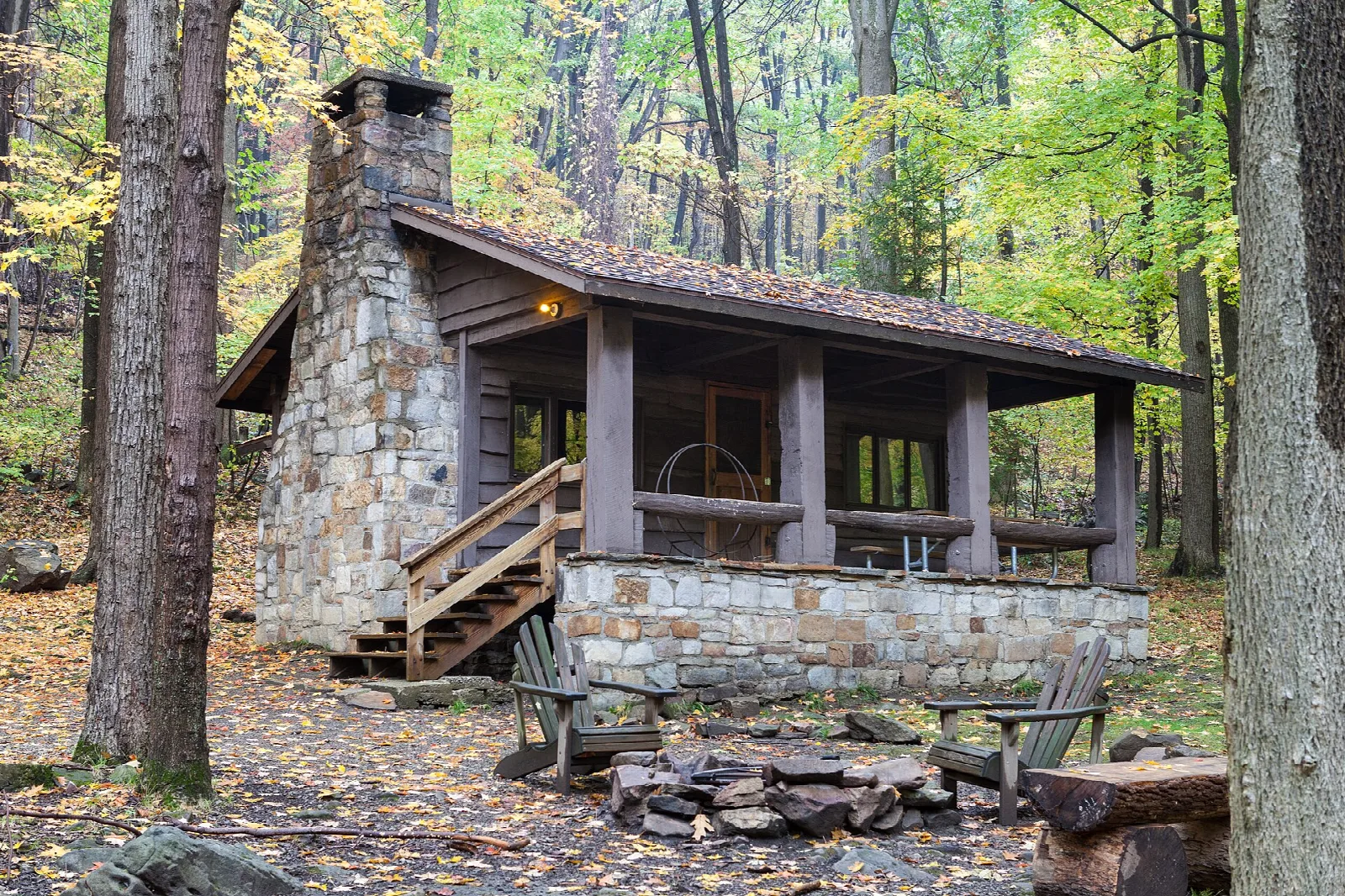 Stone and timber cabin with a covered porch among autumn trees