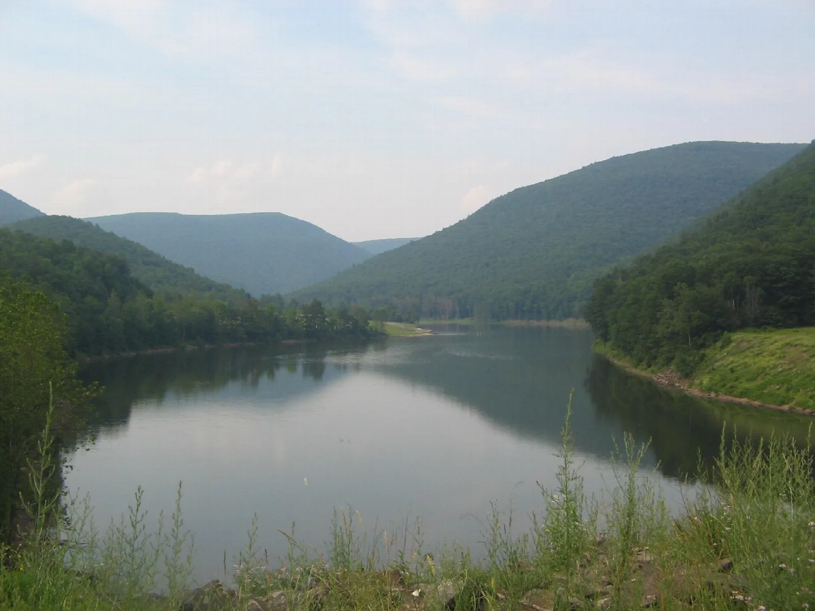 Lake between forested mountains under a hazy sky