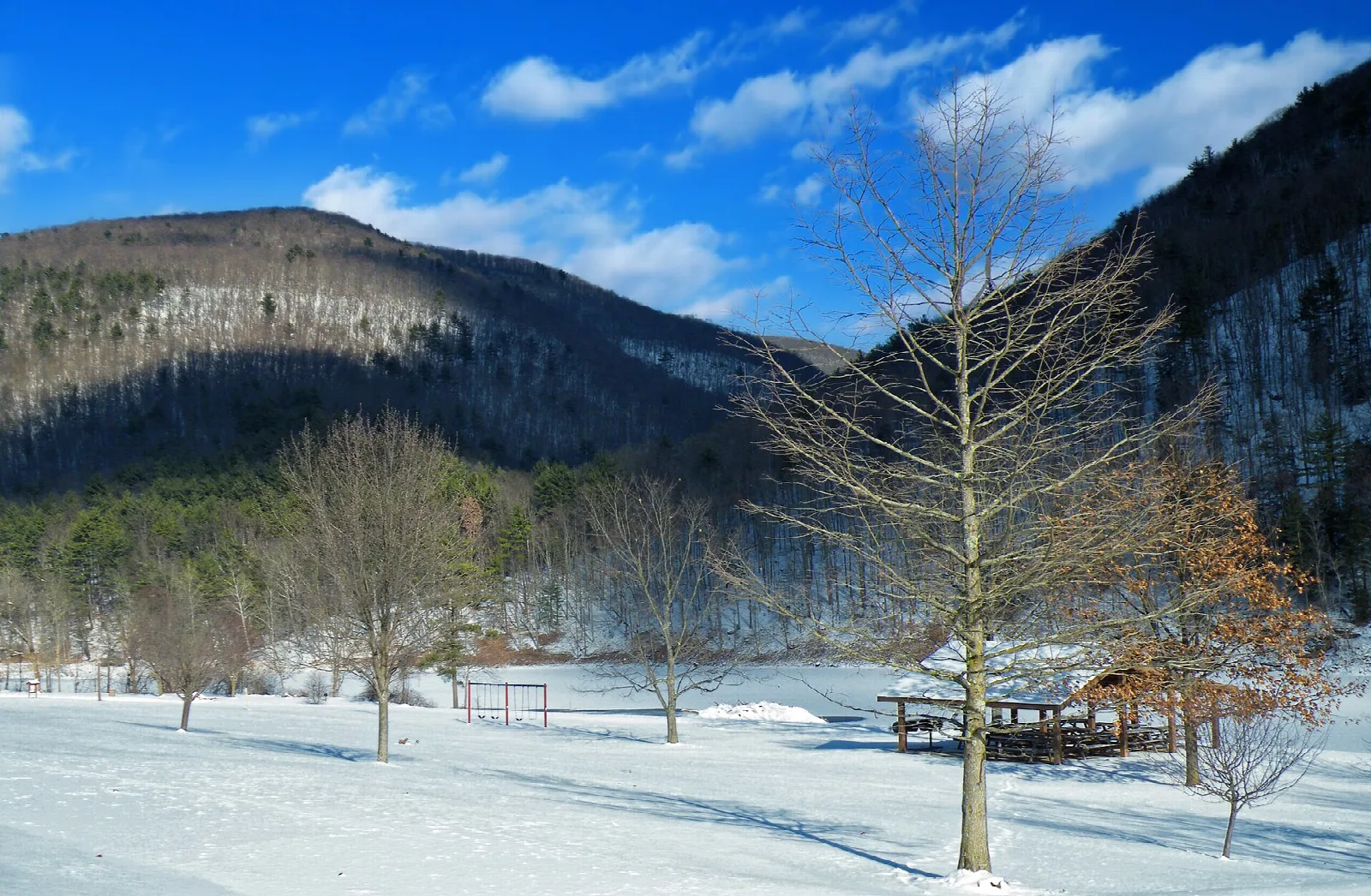 Snowy picnic area beside a lake below a wooded ridge