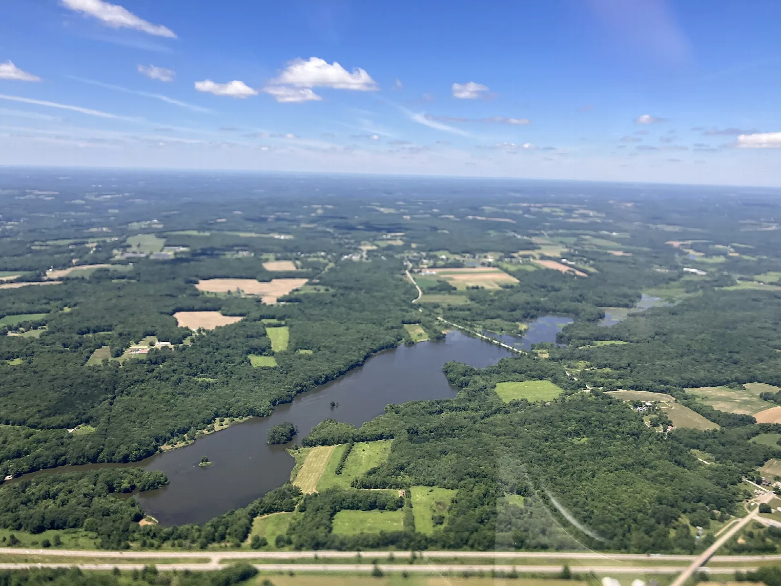 Aerial view of a long lake among farm fields and forest