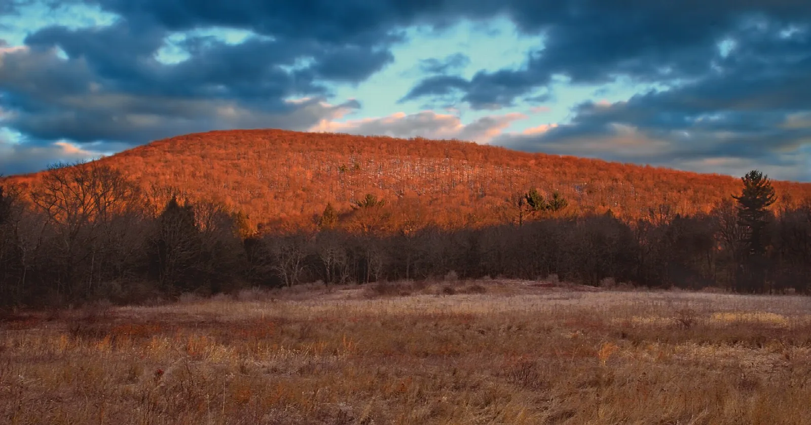 Orange-lit mountain above a dry meadow under dark clouds