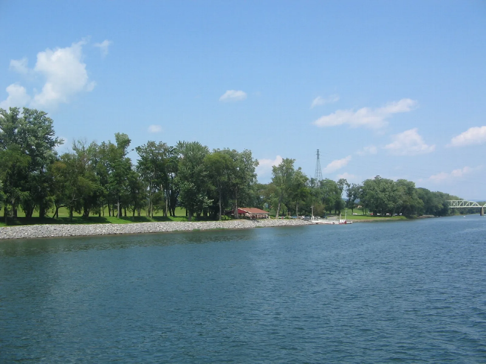 Tree-lined riverbank and blue water under a bright sky