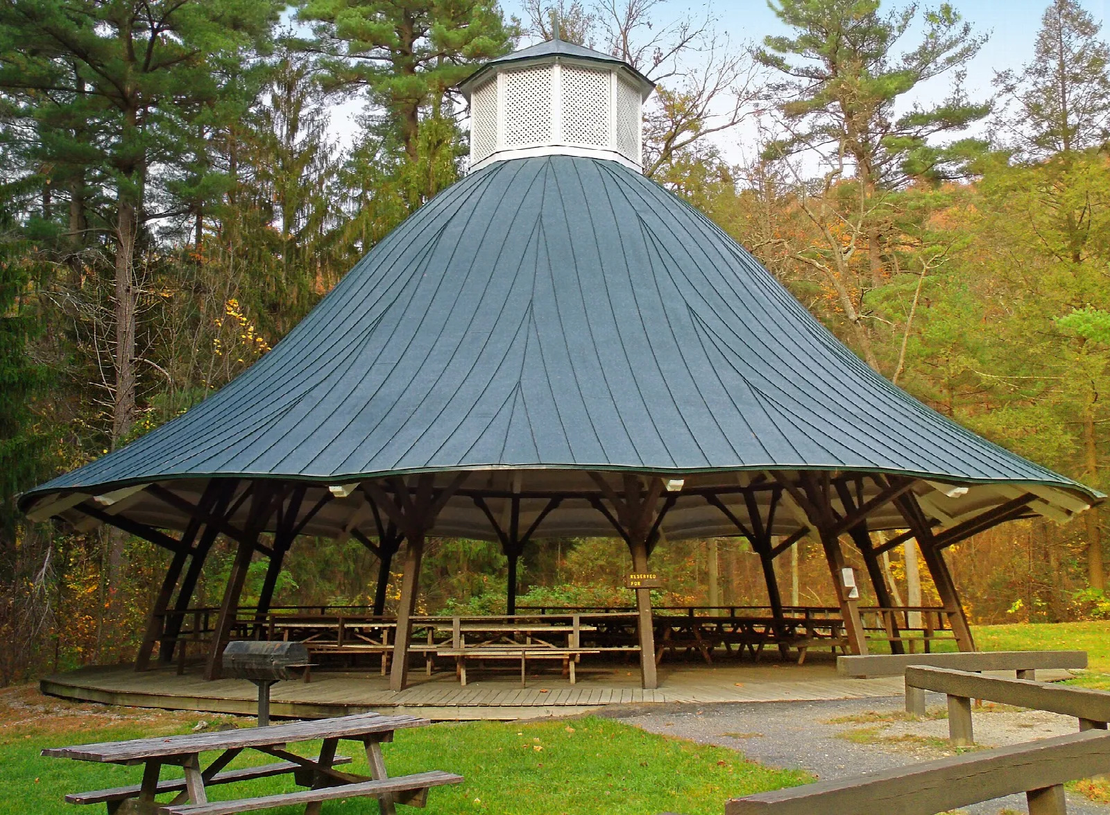 Round green-roofed pavilion with picnic tables among evergreens