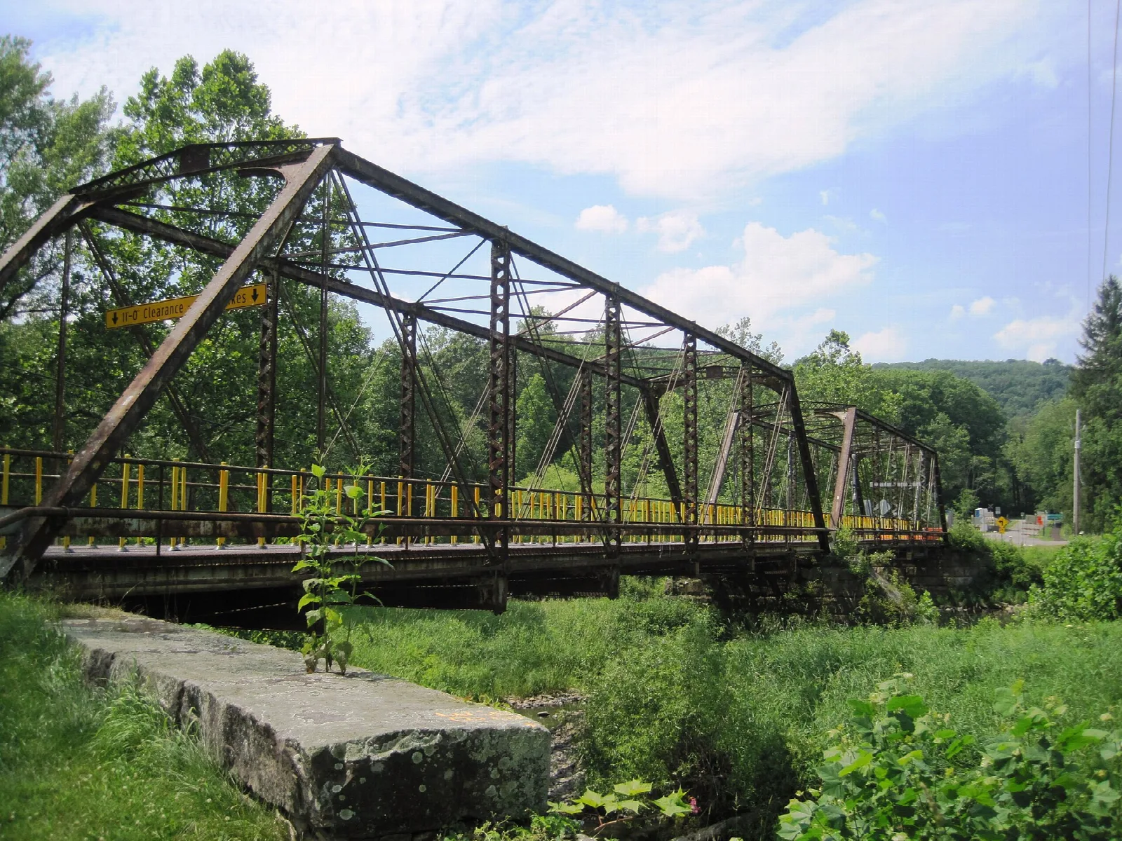 Old iron truss bridge over a creek with summer foliage