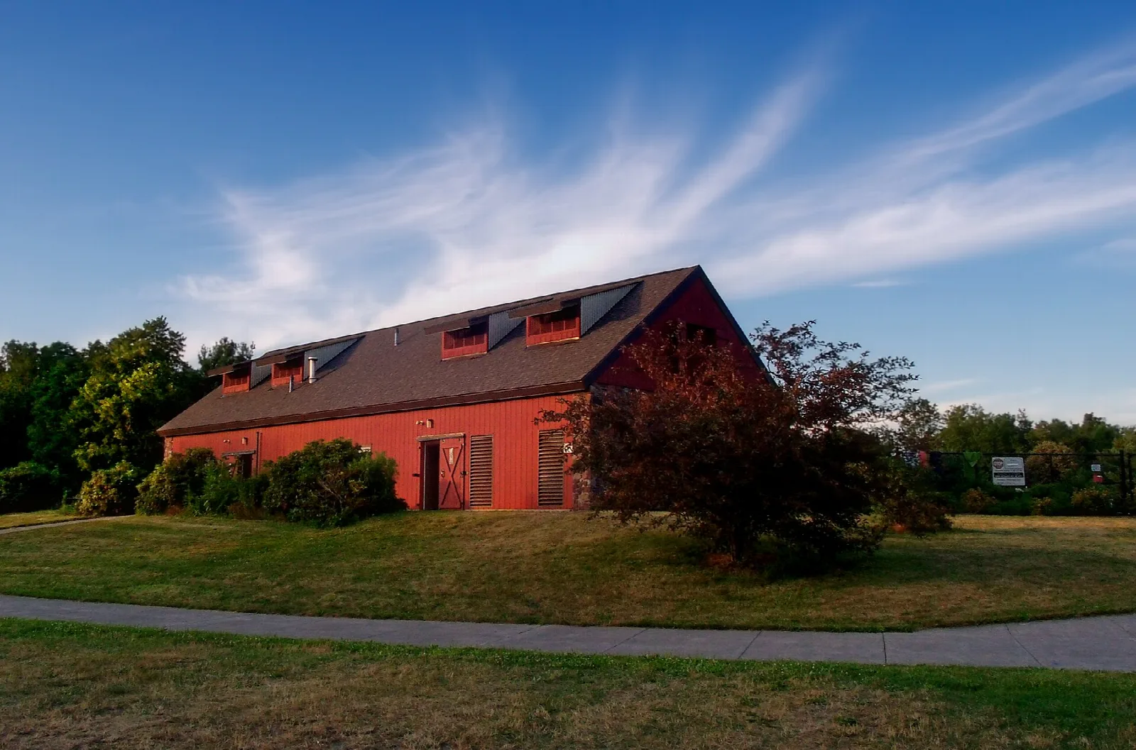 Red barn-style building on a lawn under a streaked blue sky