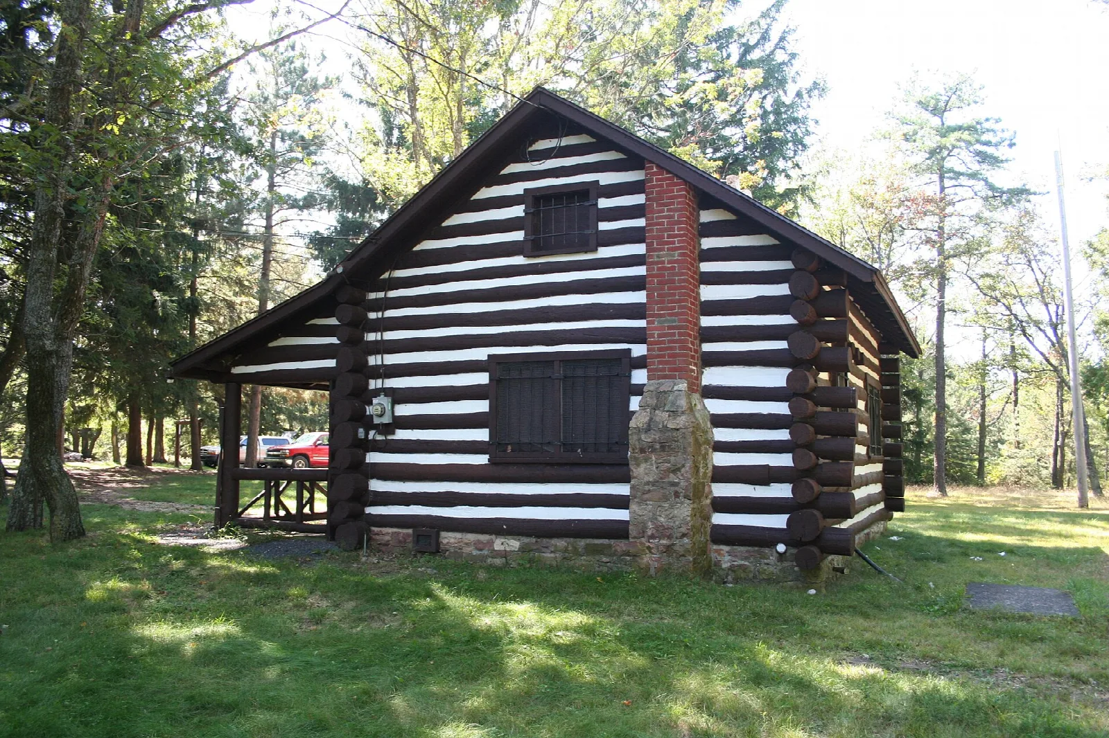 Black and white log cabin on a lawn among tall trees