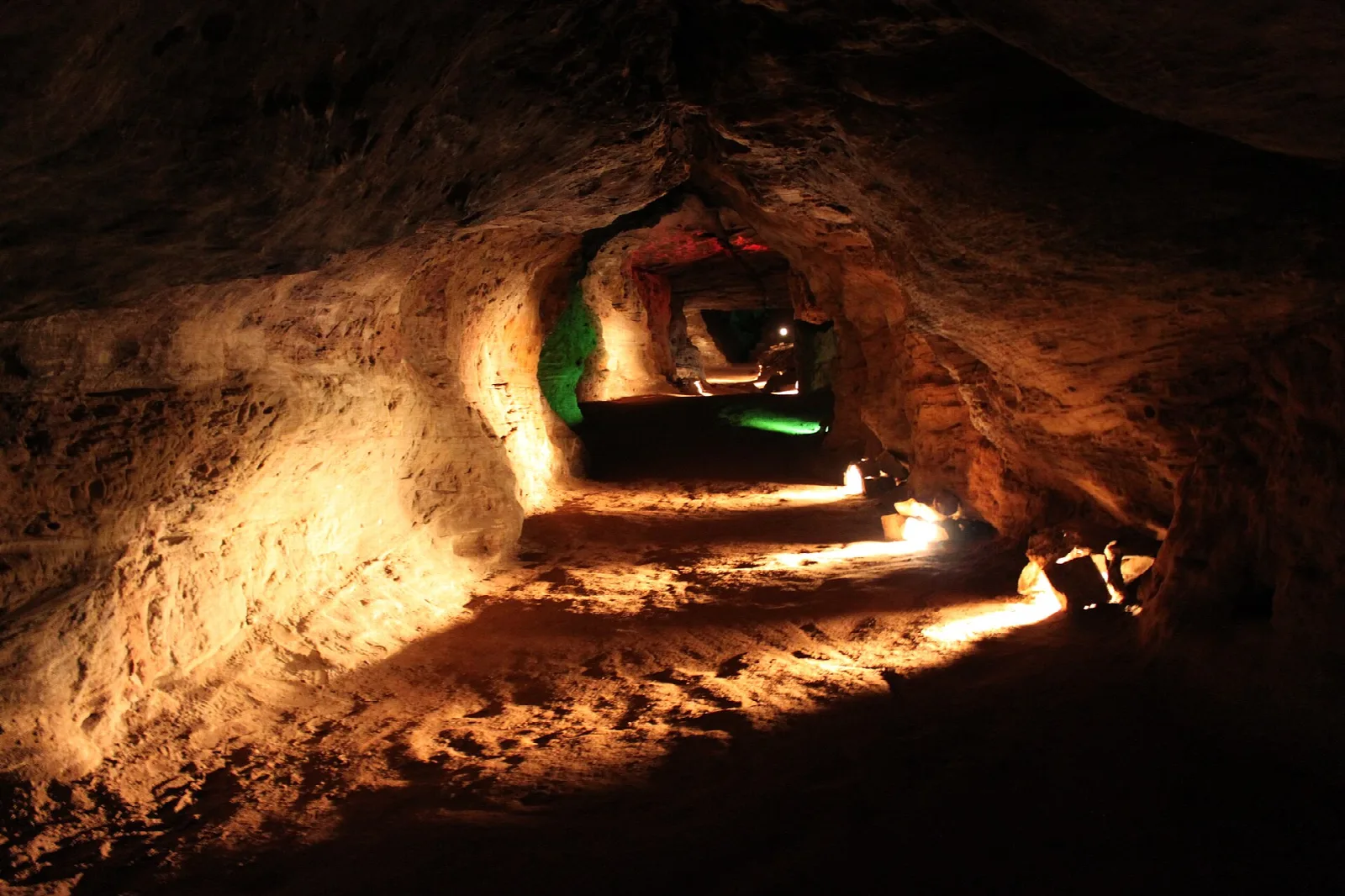 Narrow lit cave tunnel with a green light ahead