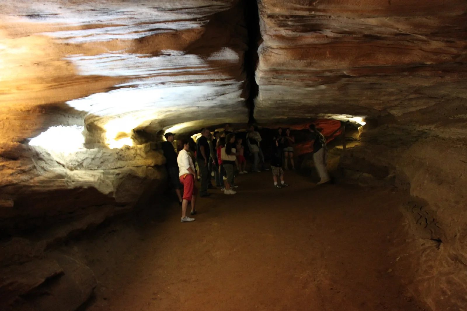 Visitors walking through a wide sandstone cave passage