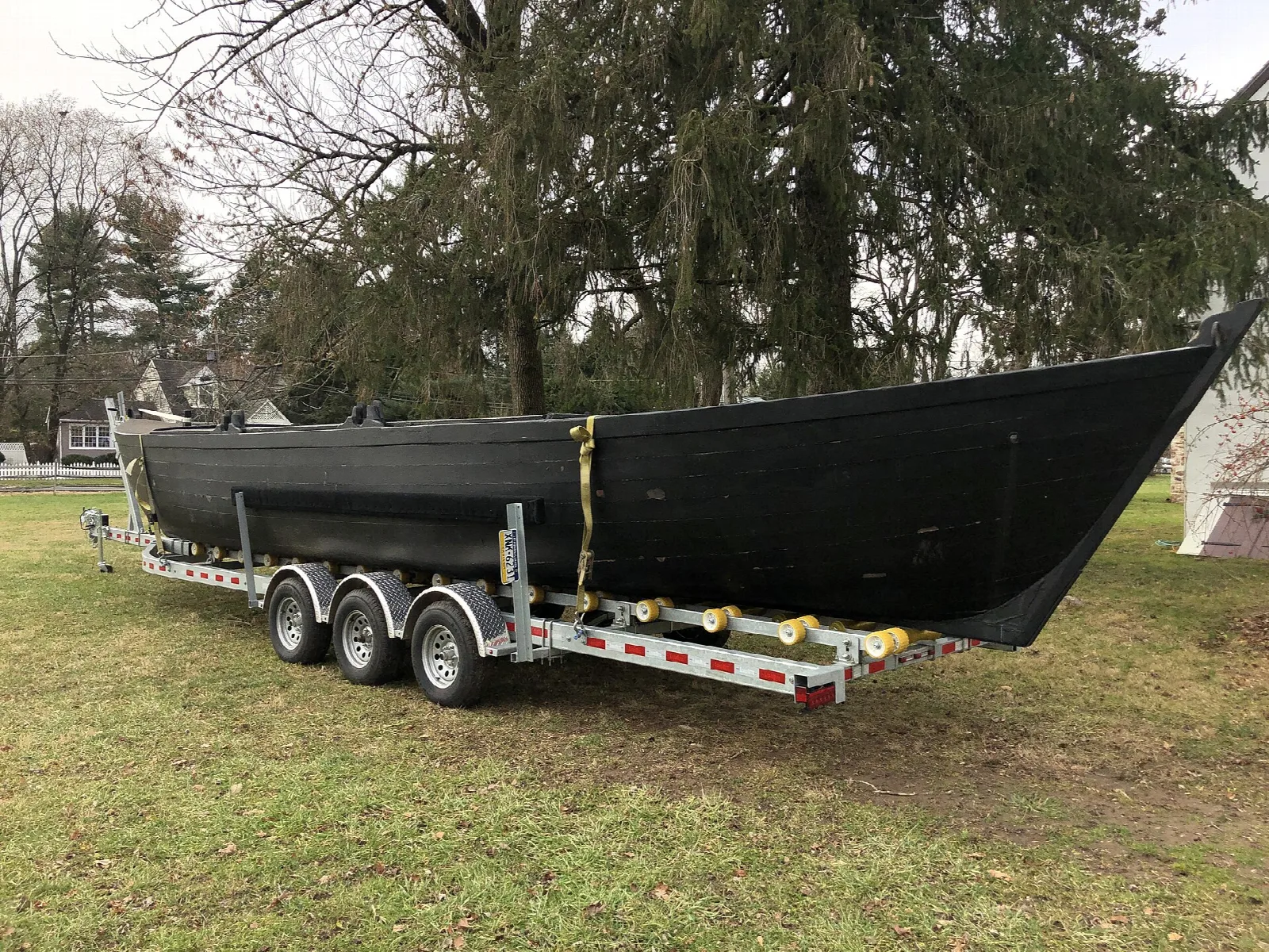 Dark Durham boat on a trailer on a lawn beneath tall trees