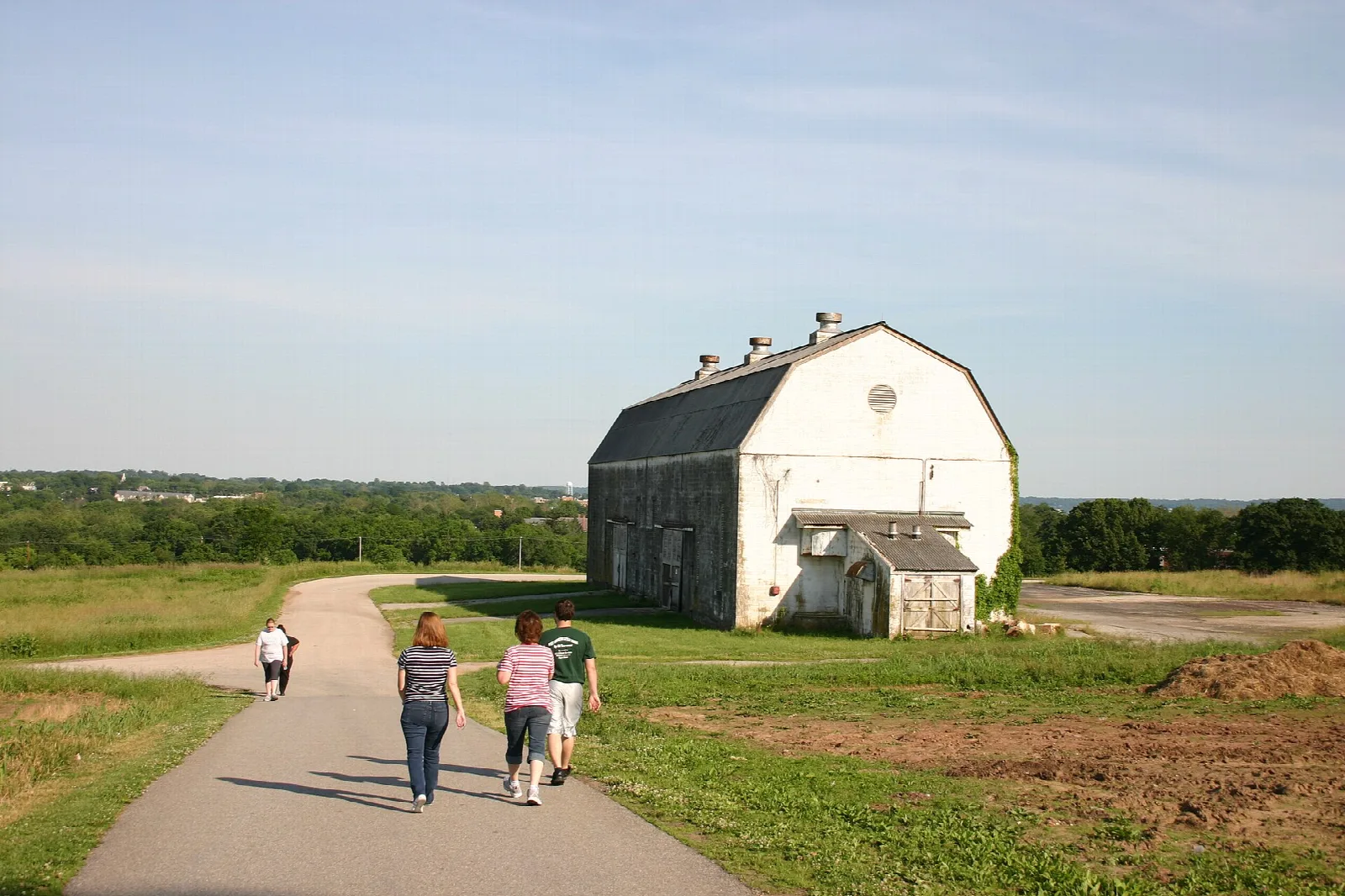 Walkers on a path toward a large white barn on a grassy hill