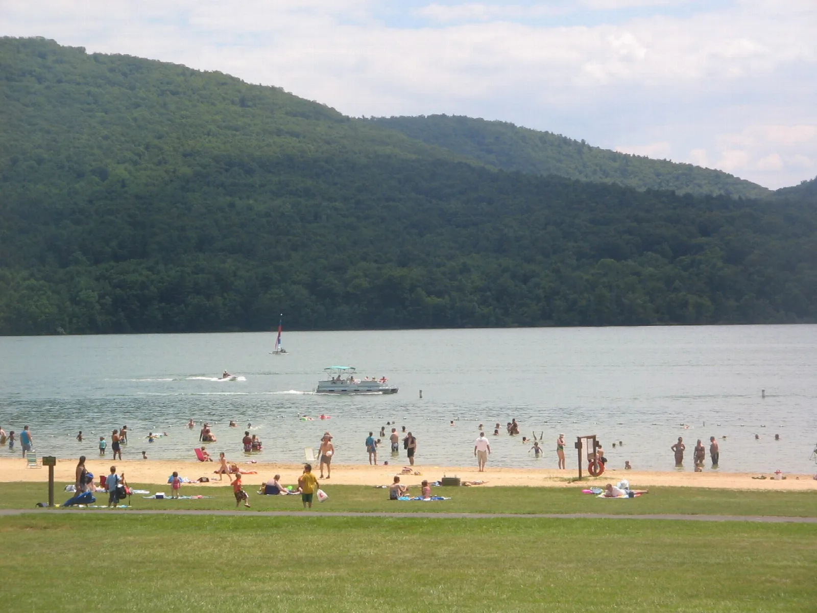 Swimmers and boats on the lake below a forested mountain