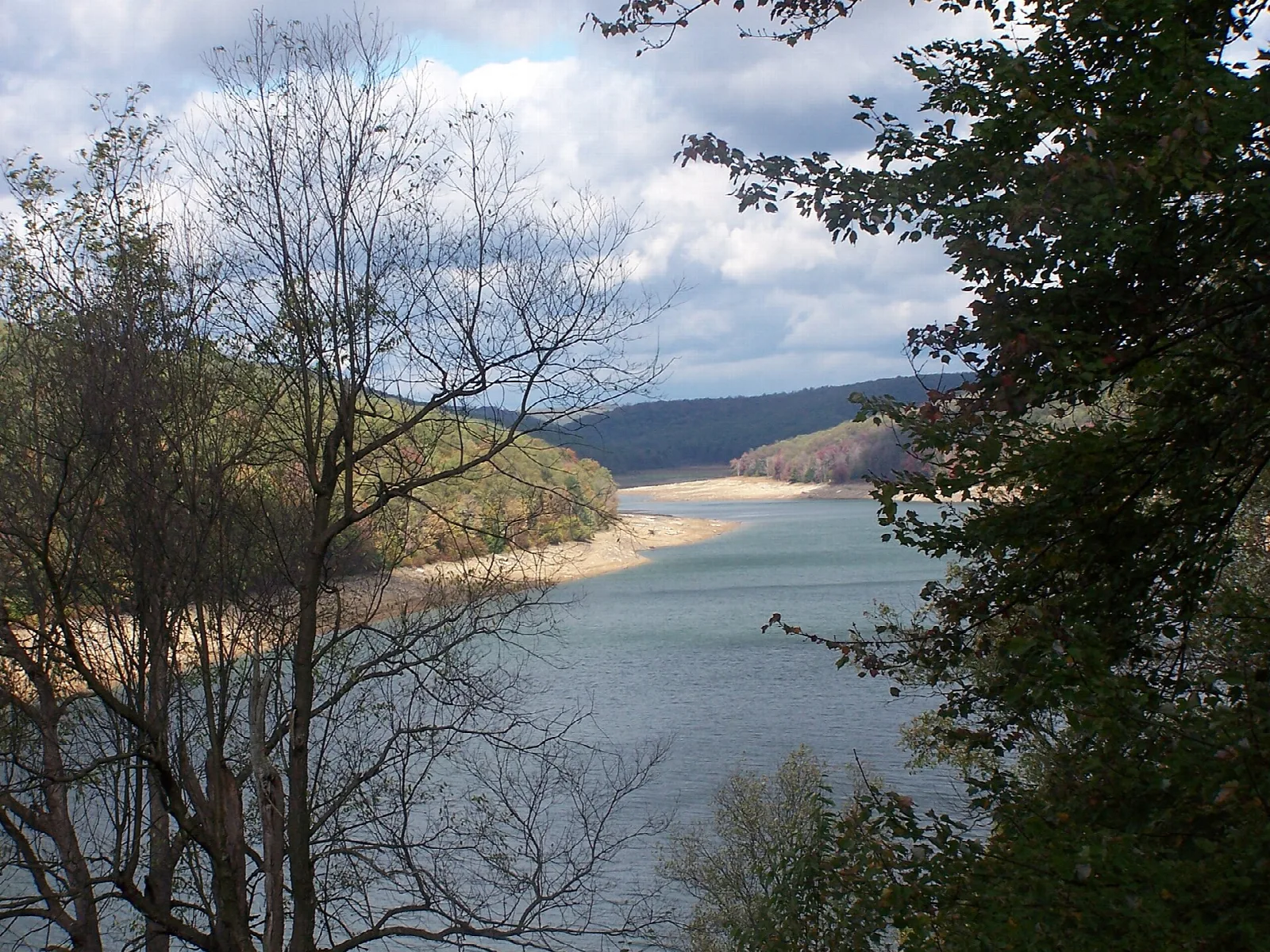 Lake with a sandy shoreline seen through bare branches, hills beyond