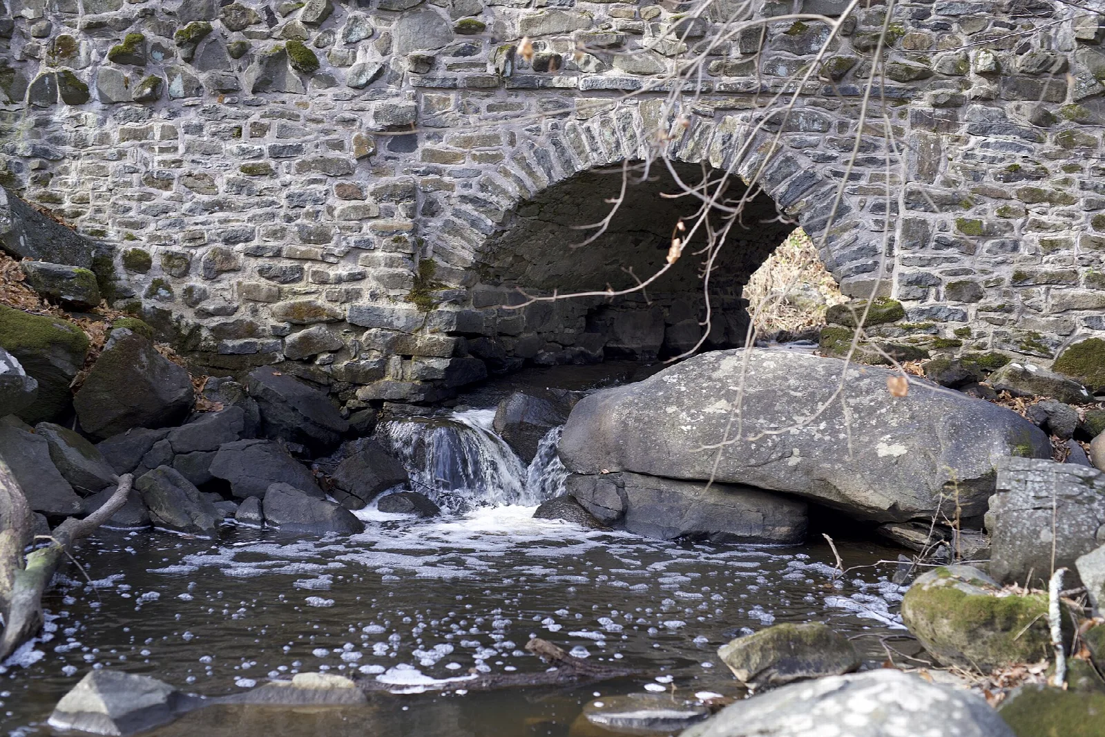 Old stone arch bridge with water spilling over rocks beneath it
