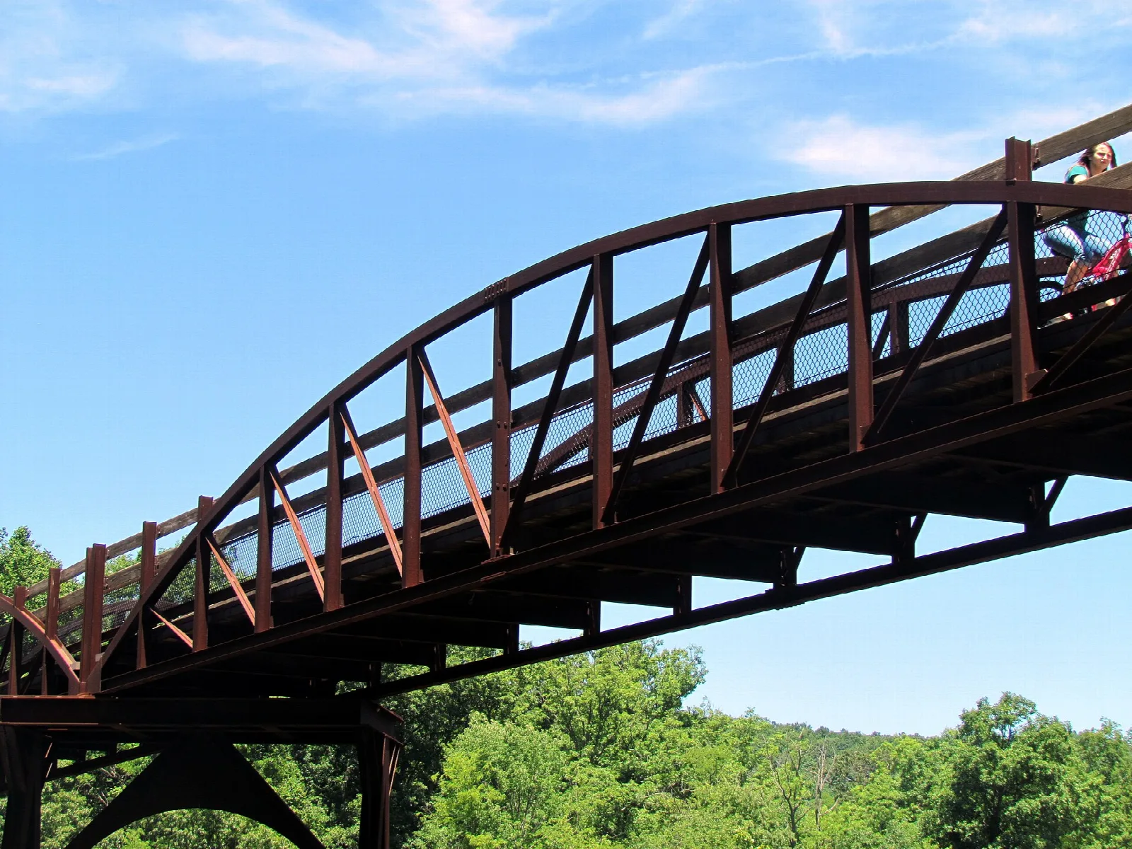 Red steel arched trail bridge against a blue sky