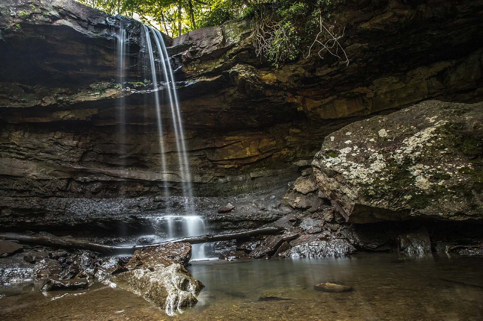 Tall thin waterfall under a rock overhang into a shallow pool