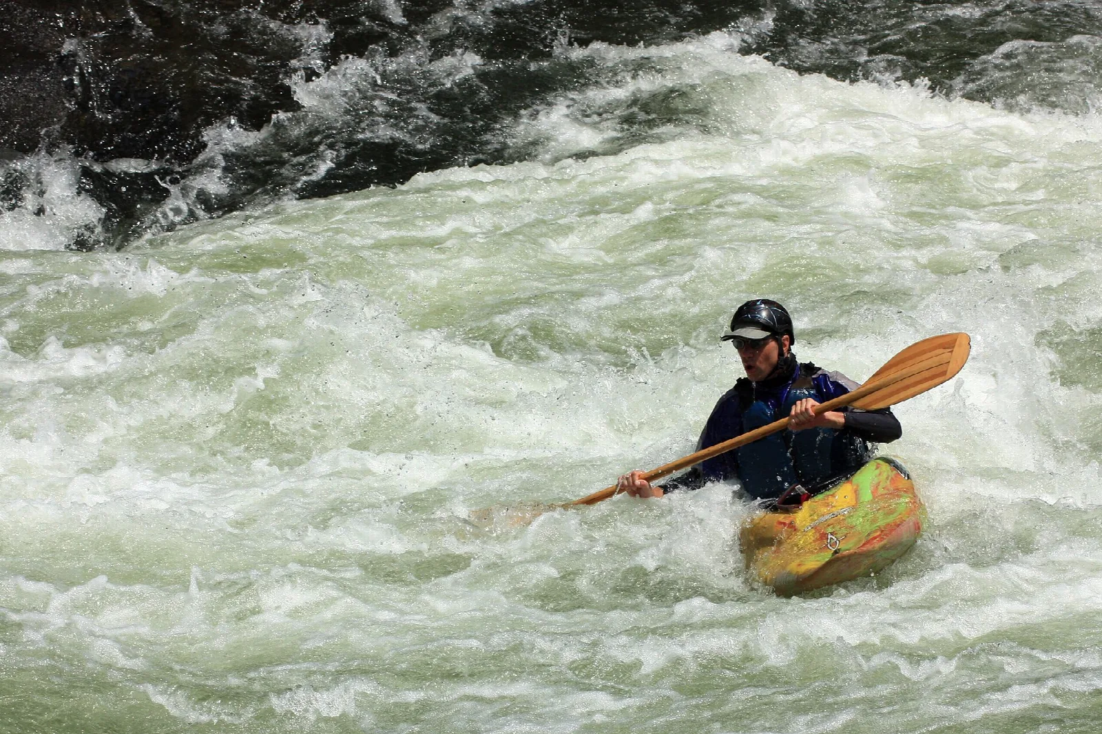 Kayaker with a wooden paddle in churning whitewater