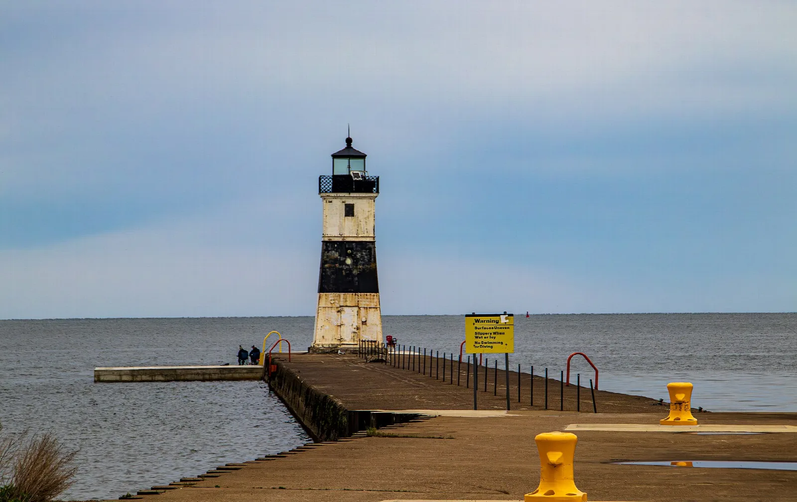 Black and white lighthouse at the end of a pier on the lake