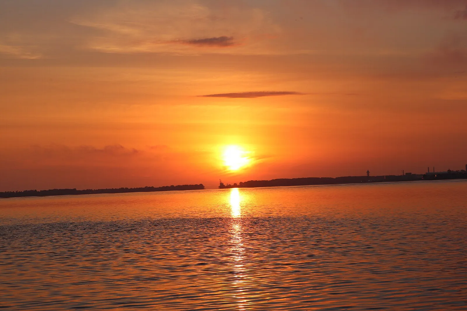 Orange sun low over a flat lake horizon with its reflection on the water