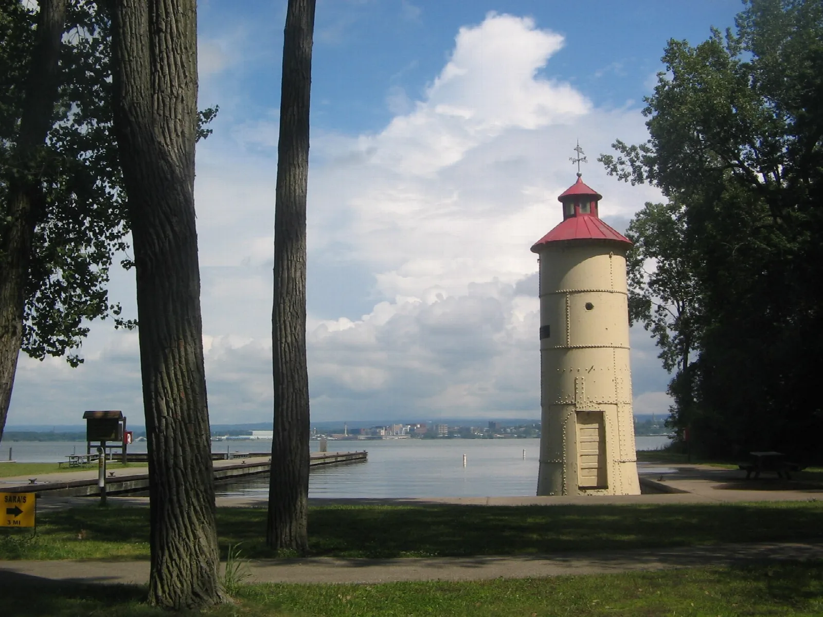 Small tan tower with a red cap among trees, bay and city in the distance