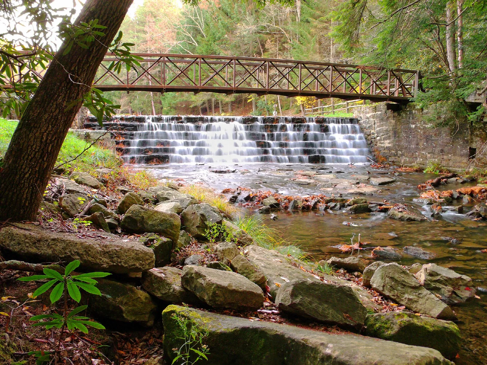 Low stone dam with a footbridge above it and rocks in the foreground