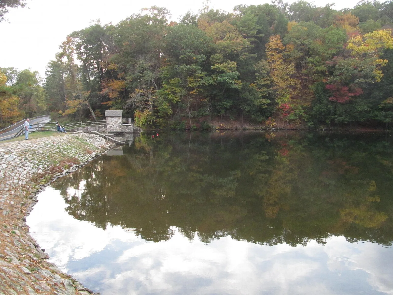 Still lake with fall trees reflected and a stone dam edge on the left