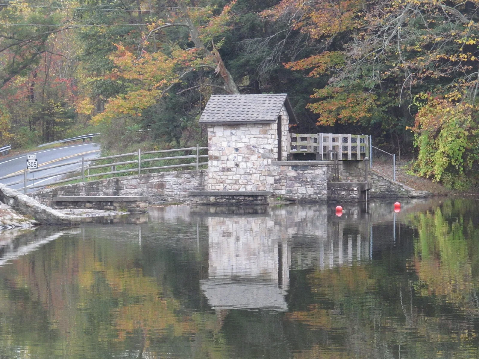 Small stone building beside still water with fall foliage behind