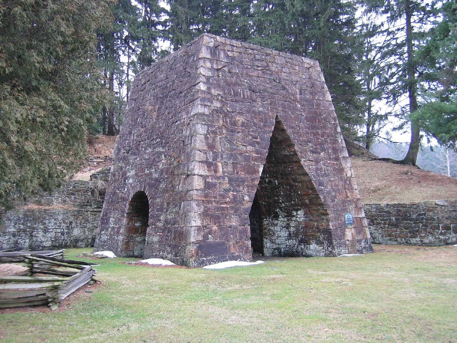 Tall stone furnace stack with an arched opening on a lawn