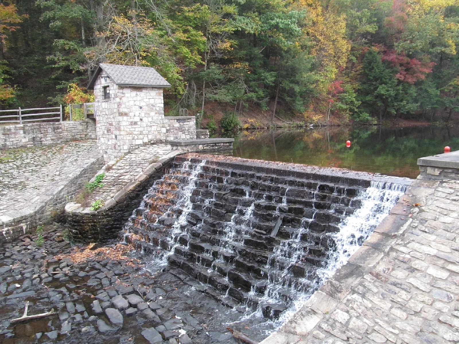 Water spilling down a stone dam beside a small stone building in fall woods