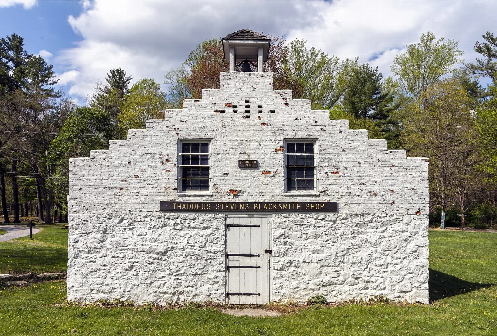 White stepped-gable stone shop building with a cupola on a lawn