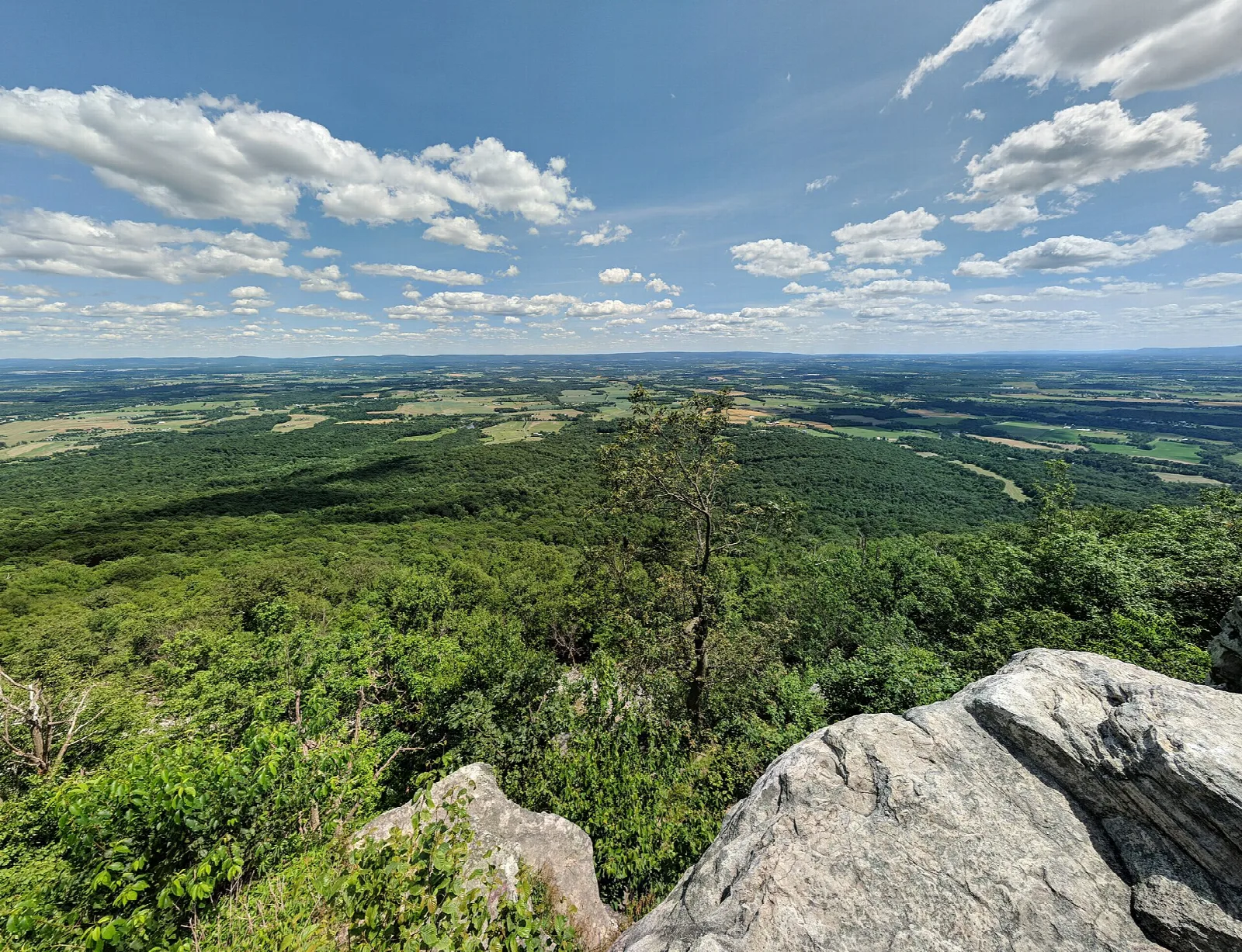 Wide farm valley seen from a rocky overlook under blue sky