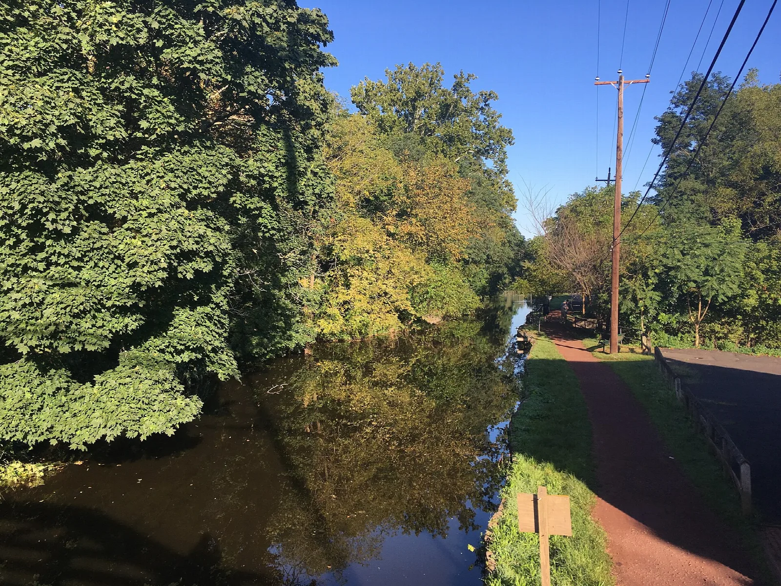 Canal under green trees beside a towpath in sunlight