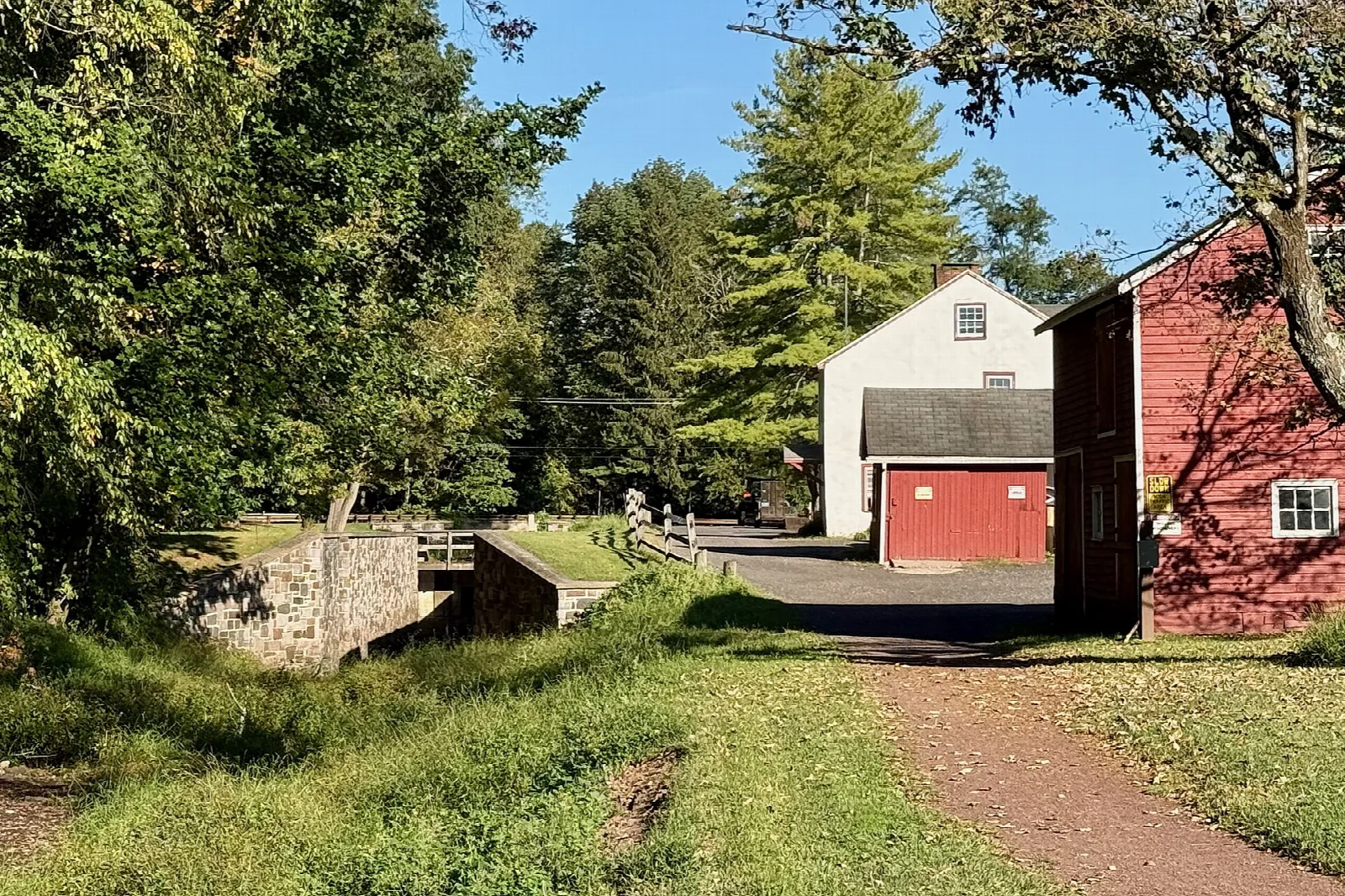 Stone lock beside a white house and red barn along the towpath