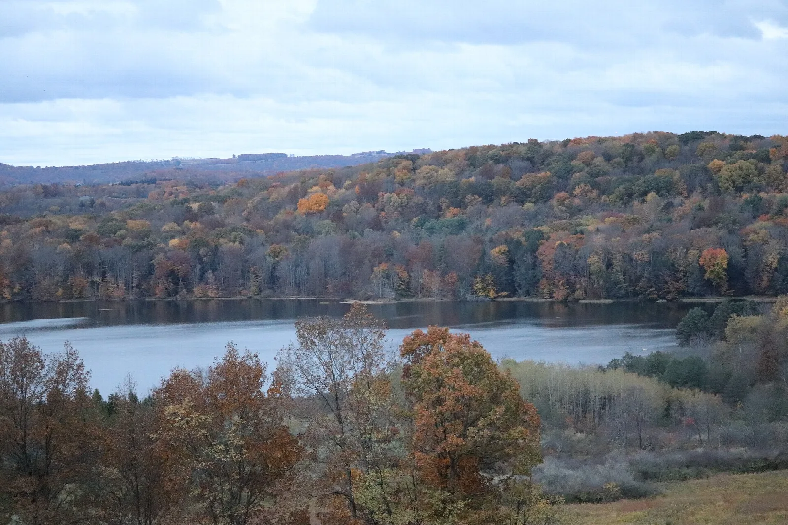 Autumn-colored hillside above a lake with clouds overhead