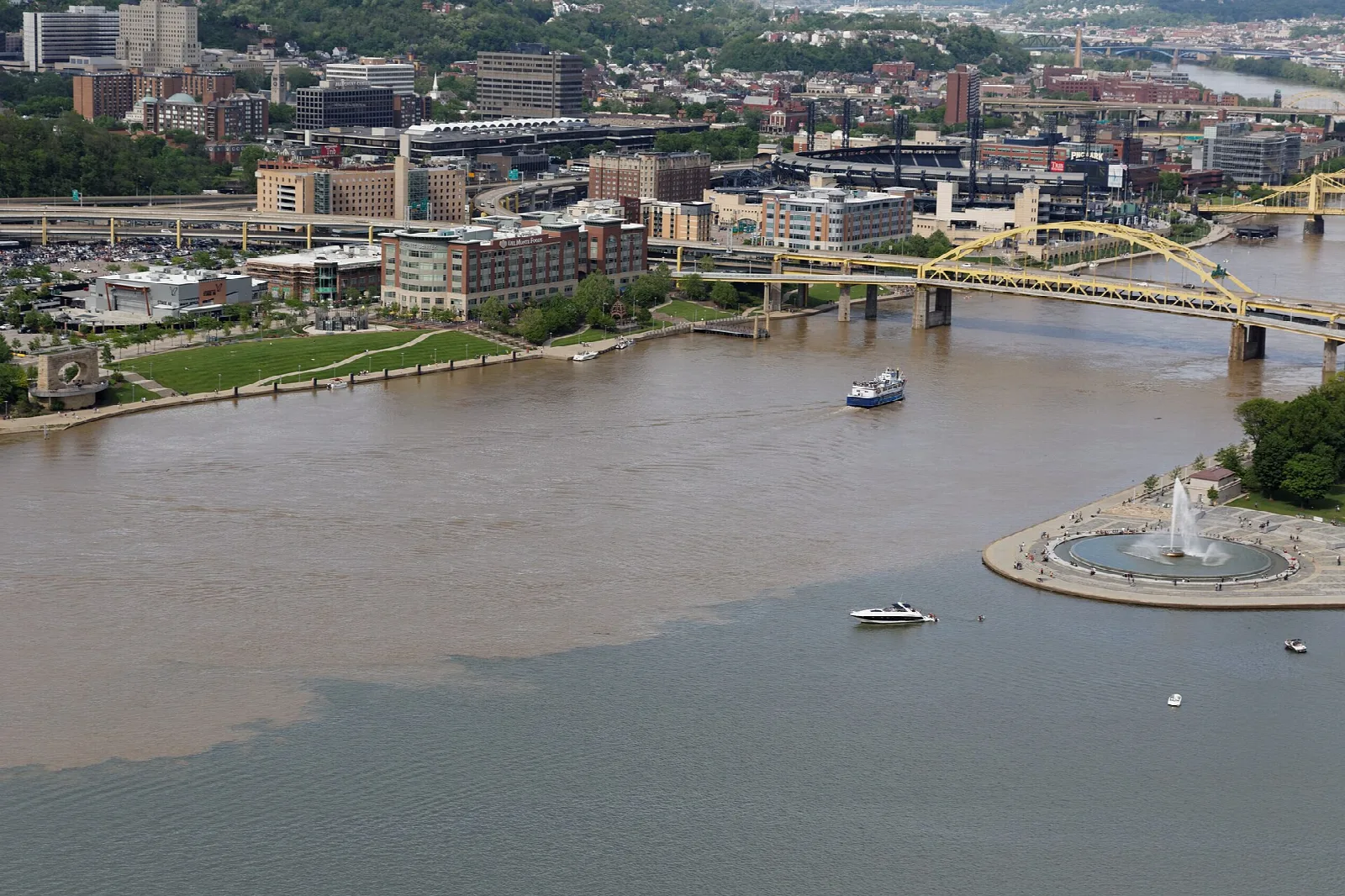 Aerial of two rivers meeting beside a park with a fountain and city buildings