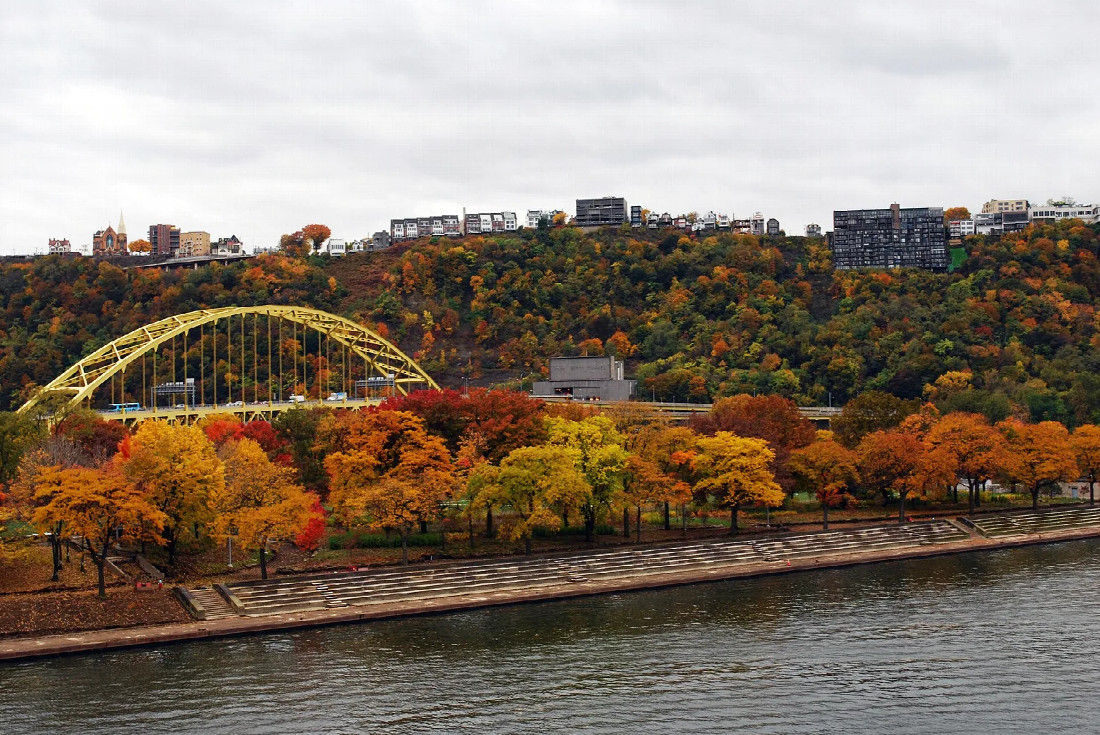 Autumn-colored trees along a riverbank below a yellow arch bridge