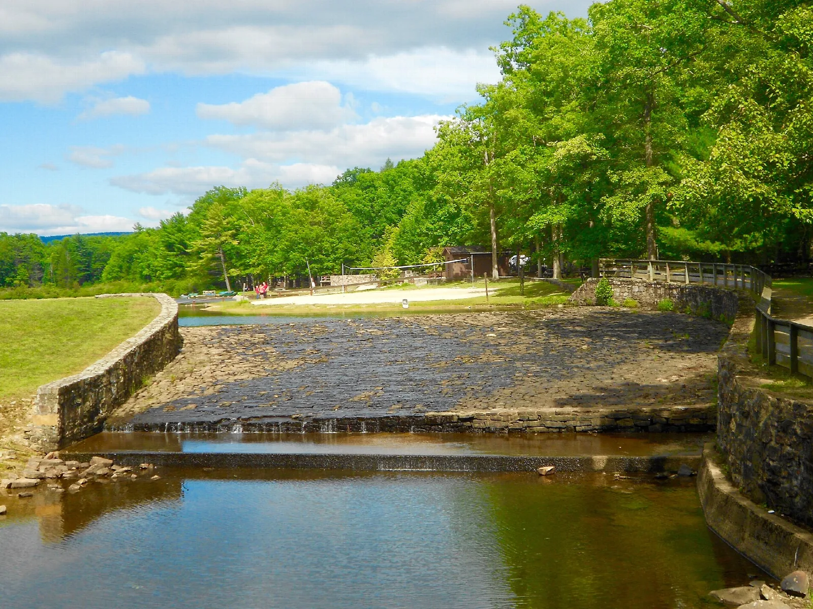 Stone-walled spillway with water flowing beside a grassy picnic area