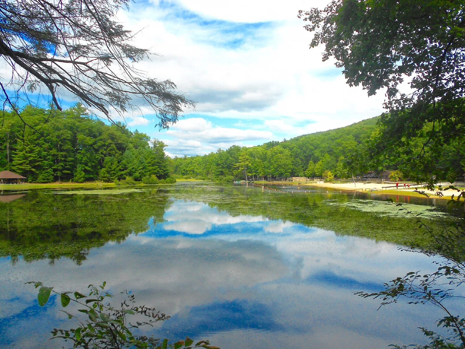 Still lake reflecting blue sky and clouds with forested hills behind
