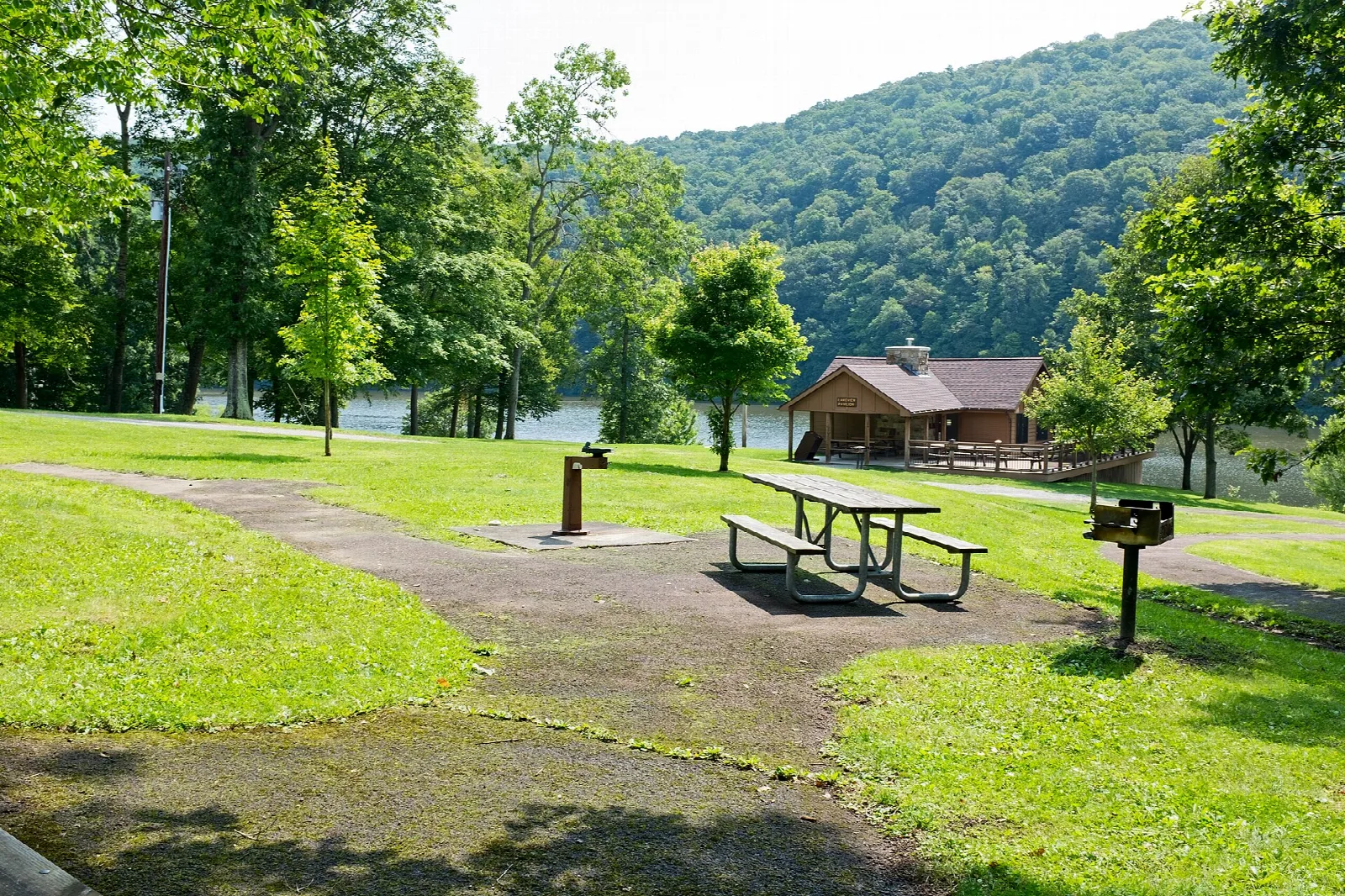 Lakeside lawn with a picnic pavilion and tables, hills across the water